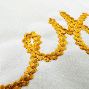 May include: A white fabric surface with the word "Love" embroidered in gold thread. The letters are formed by a series of small, connected hearts.