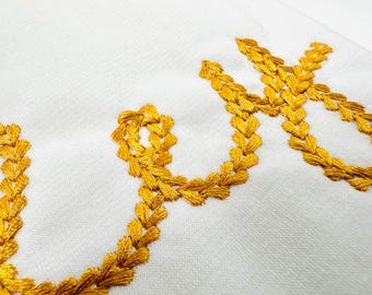 May include: A white fabric surface with the word "Love" embroidered in gold thread. The letters are formed by a series of small, connected hearts.