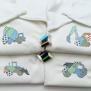 May include: Four white sweatshirts with embroidered construction vehicle designs. Each sweatshirt features a different vehicle: a cement mixer, excavator, tractor, and dump truck. The designs use a patchwork style with blue, green, and orange accents.