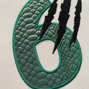 May include: Green number six with a textured, scaly surface, surrounded by three black claw marks.