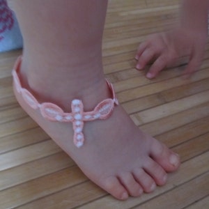 May include: A pink and white crocheted ankle bracelet with a cross design.