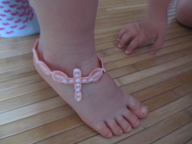 May include: A pink and white crocheted ankle bracelet with a cross design.