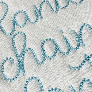 May include: Close-up of a white fabric with the words "handmade chain" embroidered in blue thread.