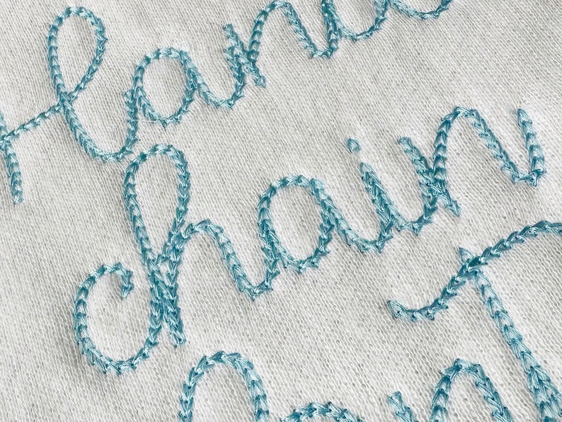 May include: Close-up of a white fabric with the words "handmade chain" embroidered in blue thread.