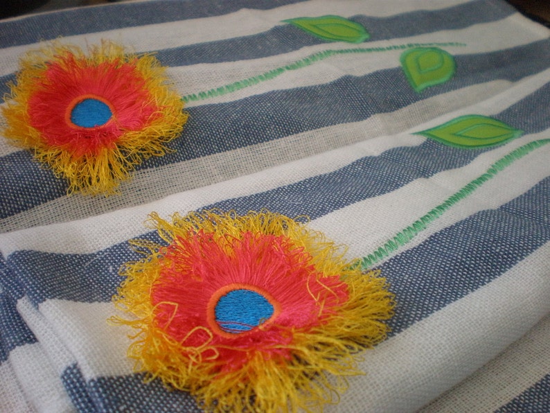 May include: Two embroidered flowers on a white and blue striped fabric. The flowers are yellow and red with a blue center.