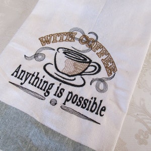 Könnte beinhalten: Weißes Küchentuch mit einem grünen Streifen am unteren Rand. Das Tuch hat ein gesticktes Design einer Kaffeetasse mit dem Text "With Coffee Anything is Possible."