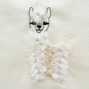 以下が含まれることがあります： 黒い目をした白い刺繍のラマ。ふわふわの白とクリーム色の体です。