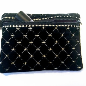 May include: A black velvet zippered pouch with gold embroidery in a diamond pattern. The pouch is partially open, revealing a black tube-shaped object inside.