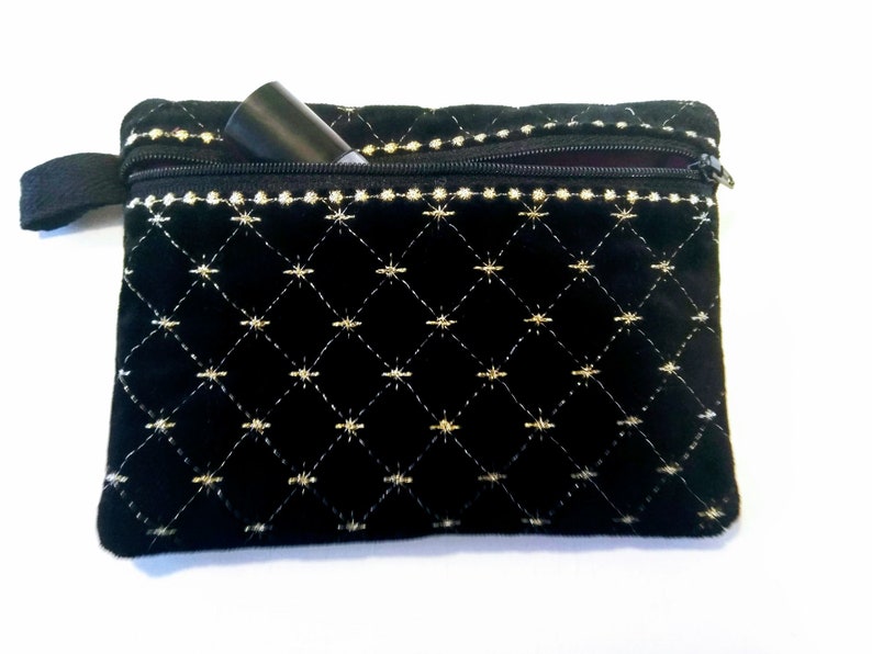 May include: A black velvet zippered pouch with gold embroidery in a diamond pattern. The pouch is partially open, revealing a black tube-shaped object inside.