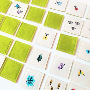 May include: A set of 20 felt squares with embroidered images of insects, butterflies, leaves, and flowers. The squares are green and white.