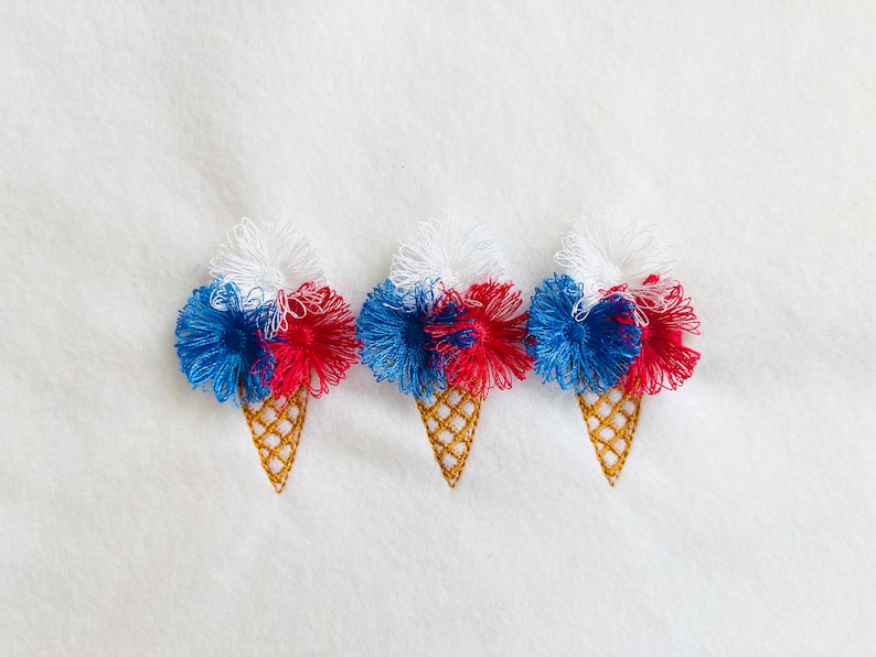May include: Three embroidered ice cream cones with red, white, and blue pom-poms on a white background.
