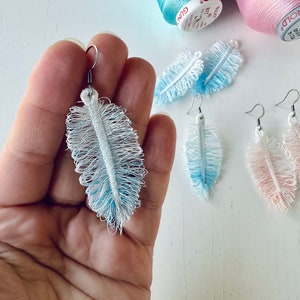 K&ouml;nnte beinhalten: Drei Paar Federohrringe in Blau, Rosa und Wei&szlig;. Die Ohrringe sind aus zartem, flauschigem Stoff gefertigt und haben einen einfachen silbernen Hakenverschluss.