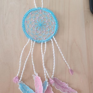 May include: A blue and white dreamcatcher with pink feathers hanging from it. The dreamcatcher is made of lace and has a beaded border. The feathers are made of fabric and have a delicate, lacy design.