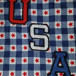 May include: A close-up of a blue and white checkered fabric with red stars. The fabric has three felt letters sewn on it that spell out "USA". The "U" is red, the "S" is white, and the "A" is blue.