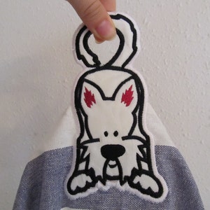 May include: White embroidered patch of a cartoon dog with black outlines and red eyes. The dog has a white body and a black nose. The patch is attached to a striped fabric.