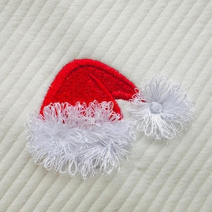 May include: A red and white embroidered Santa hat with a fluffy white trim. The hat is on a white textured background.
