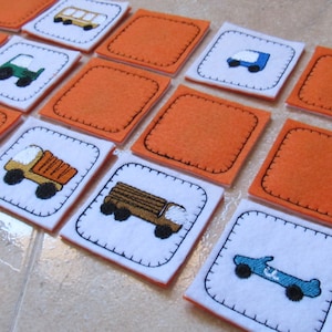Puede incluir: Un conjunto de 12 cuadrados de fieltro con pares de imágenes coincidentes. Las imágenes incluyen un camión, un automóvil, un autobús y un camión de volteo. Los cuadrados son naranja y blanco.