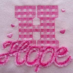 May include: Pink embroidered letter H with a gingham pattern and the word "Hope" embroidered in a pink fluffy font.