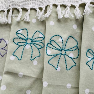 Puede incluir: Cuatro toallas de té verdes con lunares blancos y lazos turquesa bordados. Los lazos son de diferentes tamaños y están cosidos con un patrón de puntos.
