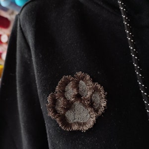 May include: A black hoodie with a brown paw print embroidered on the left side of the chest.