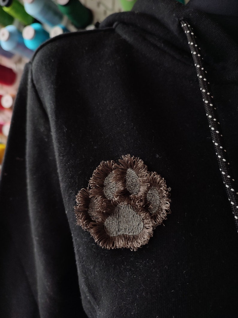 May include: A black hoodie with a brown paw print embroidered on the left side of the chest.