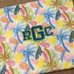 May include: White beach towel with a tropical palm tree print and the letters "RGC" embroidered in blue and green.