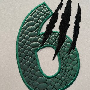 May include: Green number six with a crocodile skin texture and black claw marks.