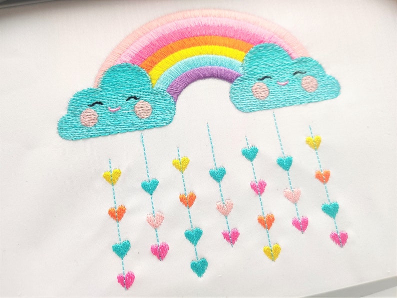 May include: Embroidered design of a rainbow with two clouds, each with a smiling face.  Hearts of various colors hang from the clouds.