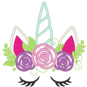 Op de afbeelding: Borduurwerk van een unicorn gezicht met een lichtblauwe spiraalvormige hoorn, roze, paarse en groene bloemen en gesloten ogen.