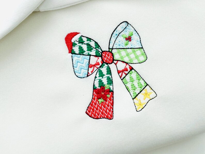 K&ouml;nnte beinhalten: Gestickte Weihnachtsschleife mit Patchwork-Design. Die Schleife hat rote, gr&uuml;ne, blaue und gelbe Abschnitte mit festlichen Mustern wie Weihnachtsb&auml;umen, Stechpalmen und Sternen. Die Schleife ist auf einem wei&szlig;en Hintergrund zentriert.