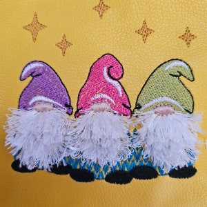 May include: Three embroidered gnomes with white beards and hats in purple, pink, and green colors. The gnomes are on a yellow background with embroidered stars.