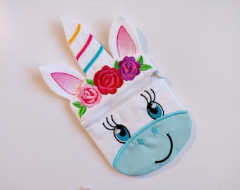 Puede incluir: Bolsa blanca con cremallera en forma de unicornio con detalles bordados. El unicornio tiene orejas rosas, un cuerno arcoíris y una cara azul con pestañas y una sonrisa. La bolsa está decorada con flores rosas, rojas y moradas.