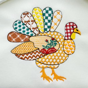 Könnte beinhalten: Gesticktes Truthahn-Design mit Patchwork-Optik. Der Truthahn hat einen rot-gelb karierten Kopf, einen gelben Schnabel und einen Fächer aus bunten Schwanzfedern. Der Körper ist eine Mischung aus gelben und orangen Mustern.