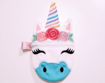 Puede incluir: Una bolsa de cremallera de unicornio blanca con una nariz azul, pestañas negras y un cuerno arcoíris. El unicornio tiene una corona de flores rosas con hojas verdes.