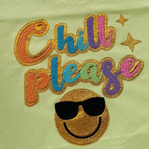 May include: A light green t-shirt with the text "Chill Please" in rainbow colors with gold glitter. A gold glitter smiley face with black sunglasses is below the text.