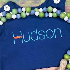 May include: A navy blue sleeveless shirt with the name "Hudson" embroidered in light blue with a small orange fish design.