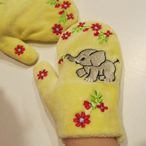 May include: A pair of yellow fleece mittens with embroidered flowers and a small elephant on one mitten.