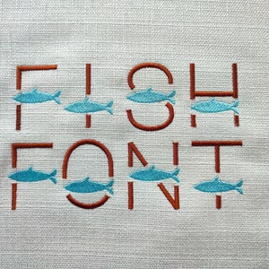 Könnte beinhalten: Ein weißer Stoff mit den Worten "FISH FONT" in braunem Garn gestickt. Jeder Buchstabe wird von einem blauen Fisch gebildet.