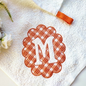 May include: White towel with an orange embroidered letter M in a scalloped circle with a white and orange gingham pattern.