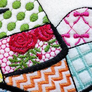 May include: A close-up of a colourful embroidered fabric with a patchwork design. The fabric features a variety of patterns, including flowers, polka dots, and geometric shapes. The fabric is stitched together with black thread.