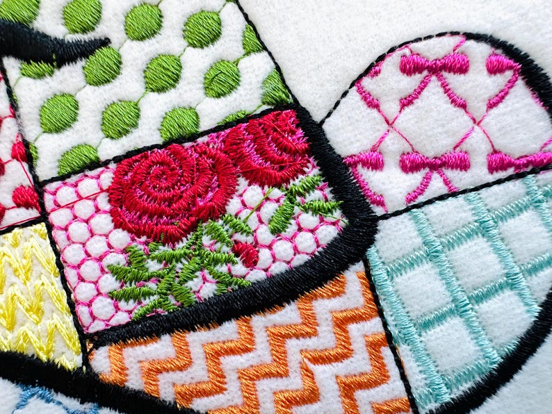 May include: A close-up of a colourful embroidered fabric with a patchwork design. The fabric features a variety of patterns, including flowers, polka dots, and geometric shapes. The fabric is stitched together with black thread.