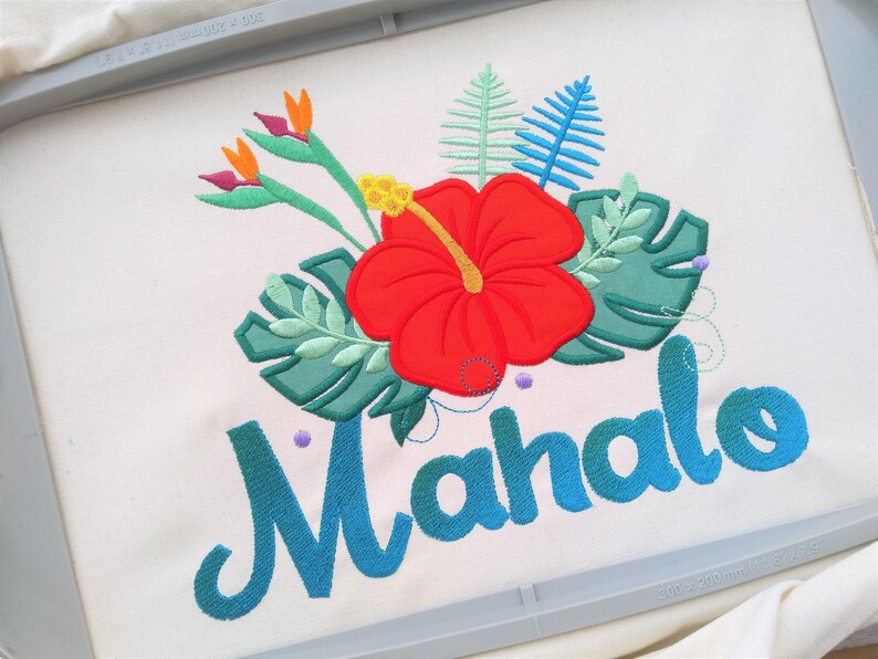 May include: Embroidered design featuring a red hibiscus flower, green leaves, and the word "Mahalo" in blue cursive lettering.