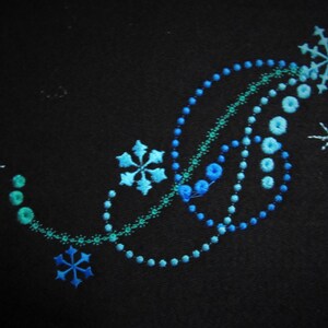 May include: Embroidered design on black fabric featuring a swirling pattern of blue and green beads, with three snowflake motifs.