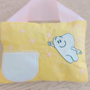 May include: A yellow tooth fairy pillow with a white pocket and a pink ribbon handle. The pillow features an embroidered tooth fairy with a wand and stars.