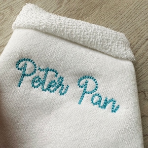 May include: White towel with blue embroidered text that reads "Peter Pan".