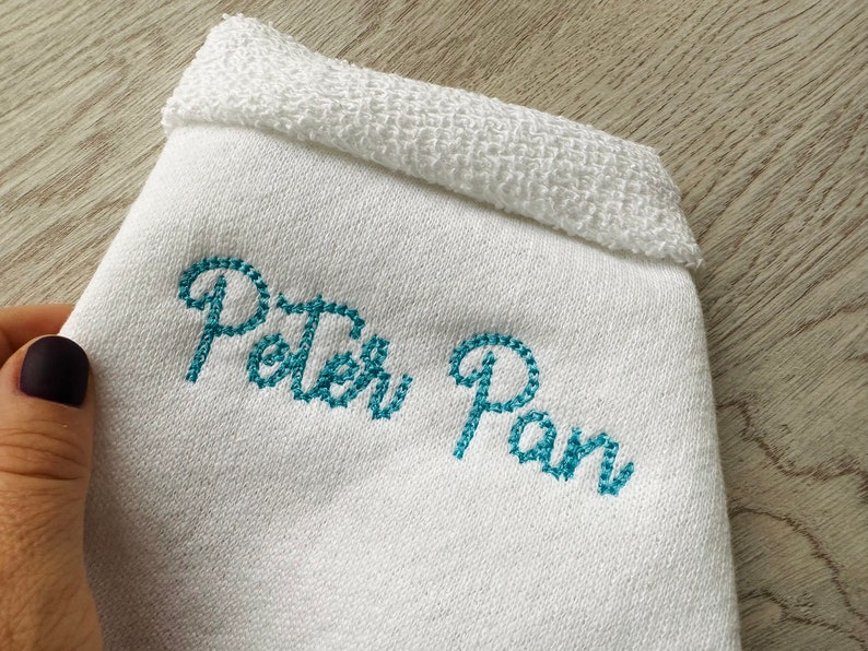 May include: White towel with blue embroidered text that reads "Peter Pan".