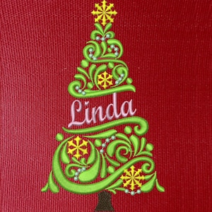 May include: Green embroidered Christmas tree with a white star on top and the name Linda in pink cursive lettering.