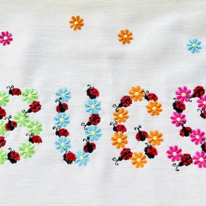 May include: Embroidered kitchen towel with the word "BUGS" spelled out in colorful flowers and ladybugs.