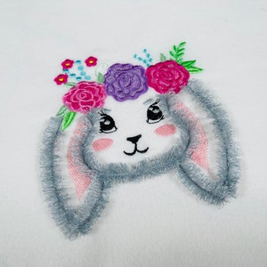 May include: Embroidered bunny with gray fluffy ears and a pink, purple, and white flower crown.