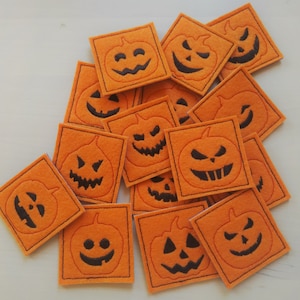 May include: A collection of 13 orange felt patches with black embroidered jack-o'-lantern faces. The patches are various sizes and shapes.